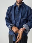 Person wearing a blue denim jacket and brown gloves on a plain background